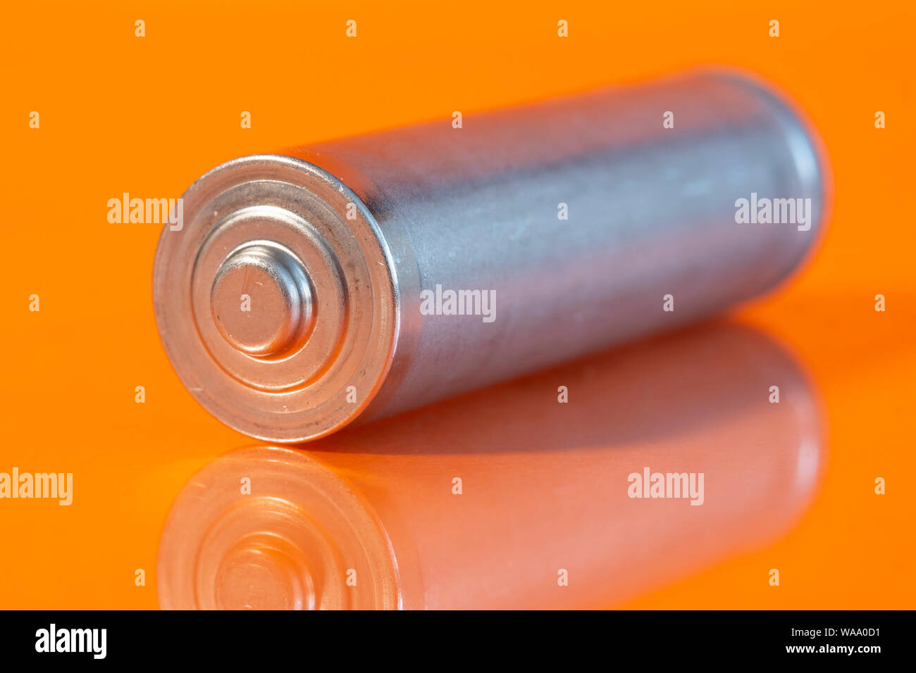 Uso singola batteria AA alcalina è visto su un arancione Riflettente superficie. Primo piano vista laterale dal lato più della batteria. Foto Stock