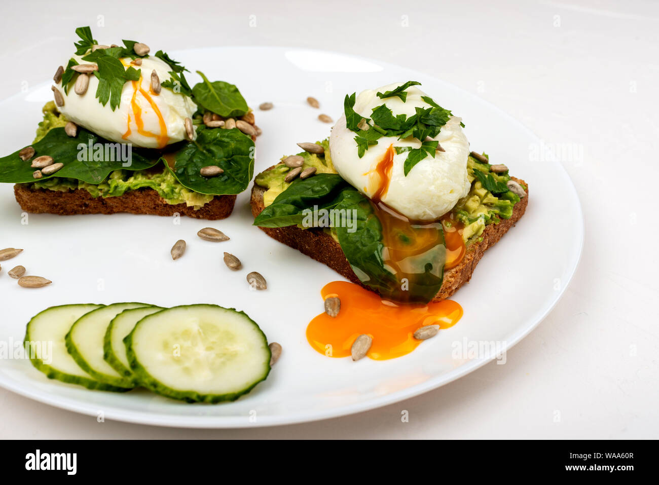 Uova al tegame con avocado, spinaci in foglie e semi su crostini di pane su una piastra bianca su sfondo bianco. Sana colazione o uno spuntino. Foto Stock