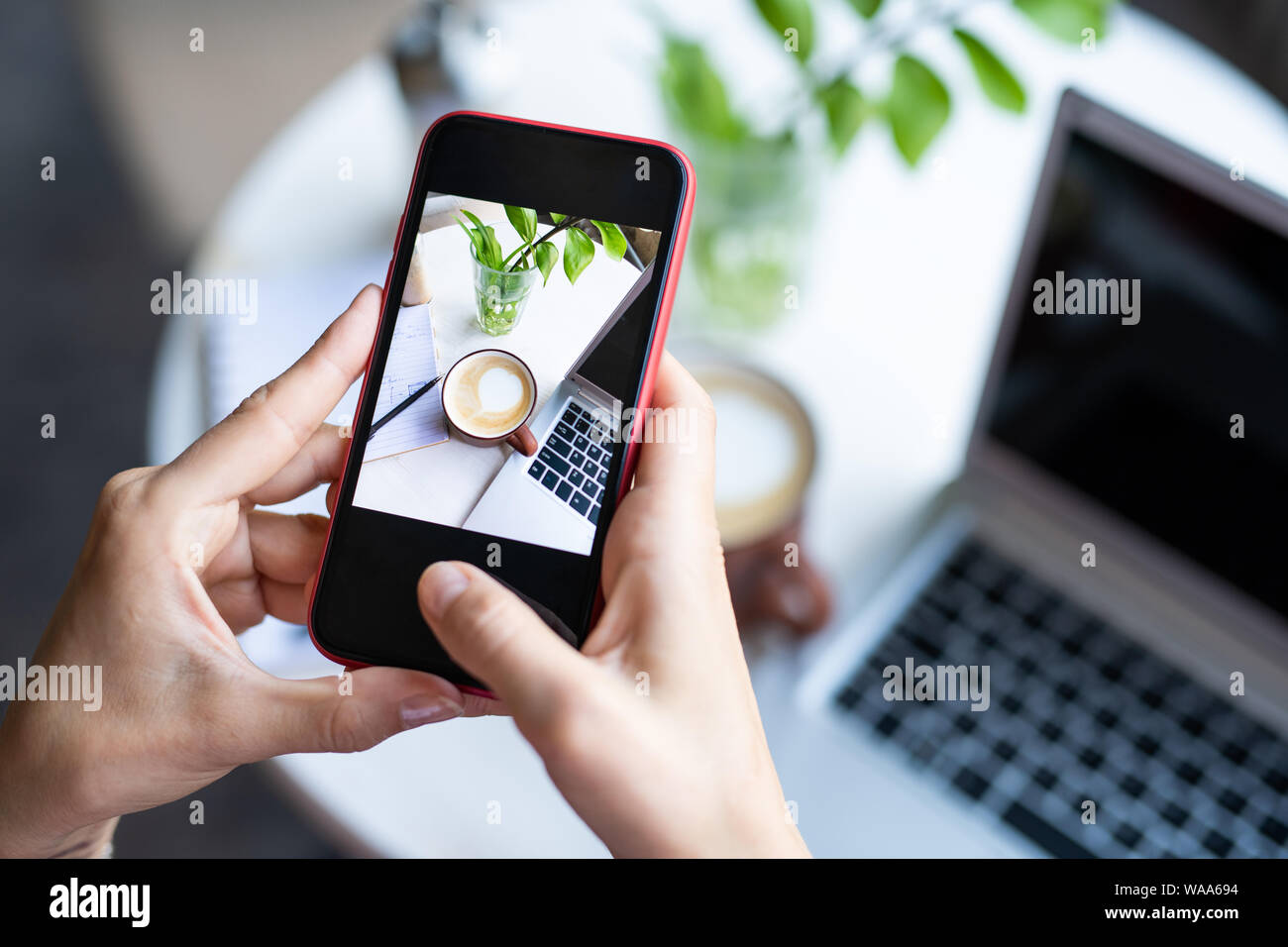 Femmina mobile prendendo la foto del cappuccino in tazza e tastiera portatile sul tavolo Foto Stock