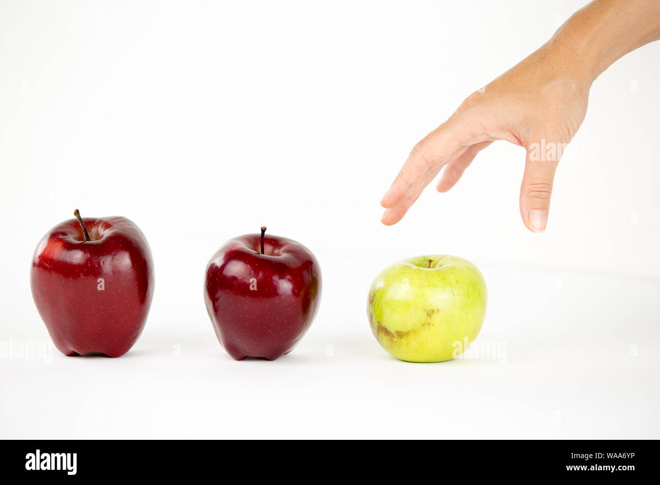 Concetto di diversità: una donna di mano è circa di agguantare il solo verde apple tra gli altri quelli rossi Foto Stock