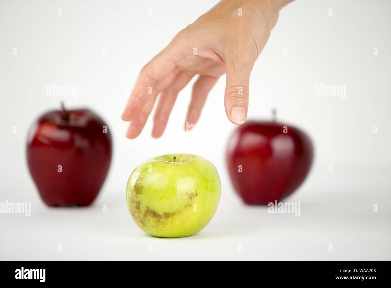 Concetto di diversità: una donna di mano è circa di agguantare il solo verde apple tra gli altri quelli rossi Foto Stock