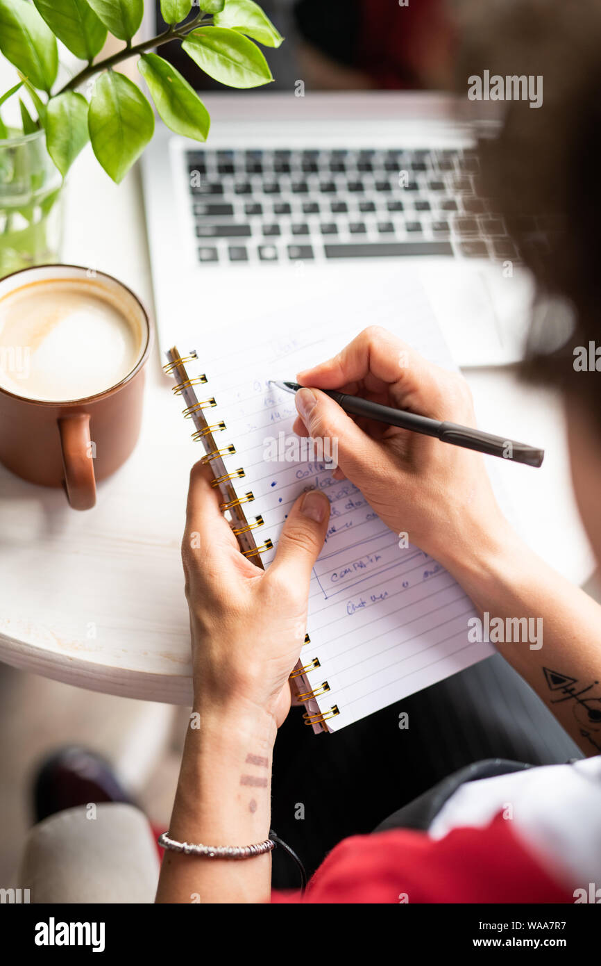 Giovane donna manager rendendo note in notebook mentre organizzazione del lavoro Foto Stock