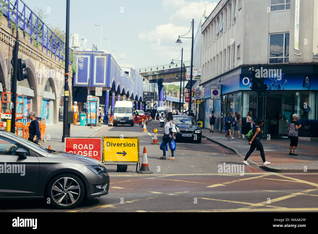 London / UK - Luglio 16, 2019: persone attraversando Atlantic Road verso Coldharbor Lane; Brixton stazione ferroviaria sulla sinistra Foto Stock