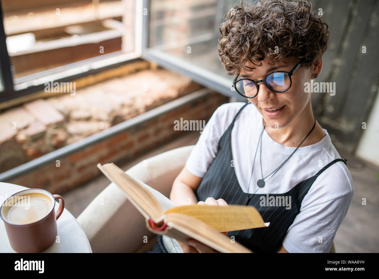 Giovane donna con brevi parentesi capelli castani e libro di lettura a casa Foto Stock