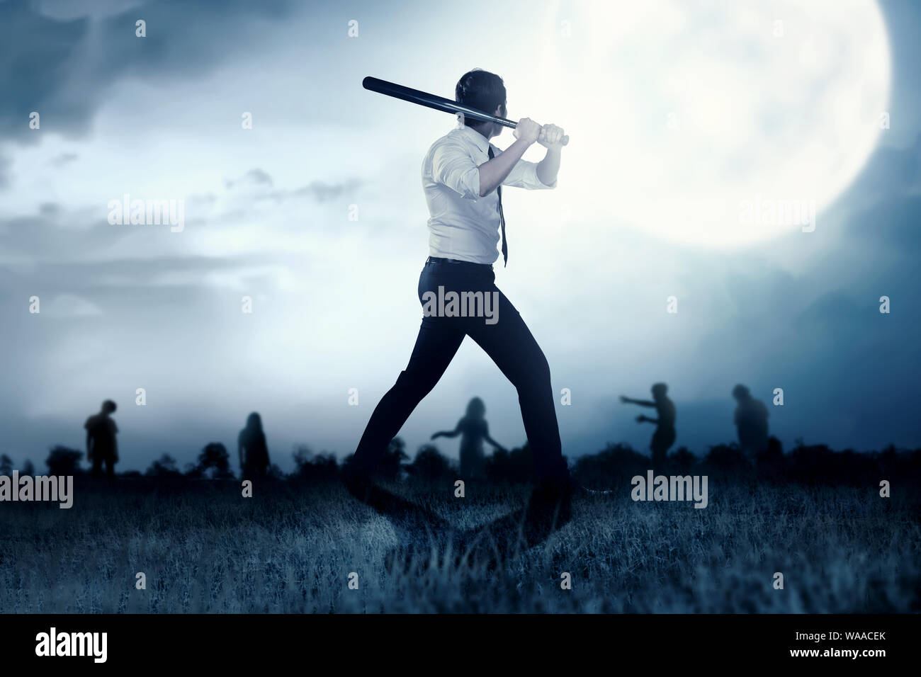 Imprenditore asiatico con una mazza da baseball sul suo volto a mano gli zombie sul campo in erba di notte. Concetto di Halloween Foto Stock