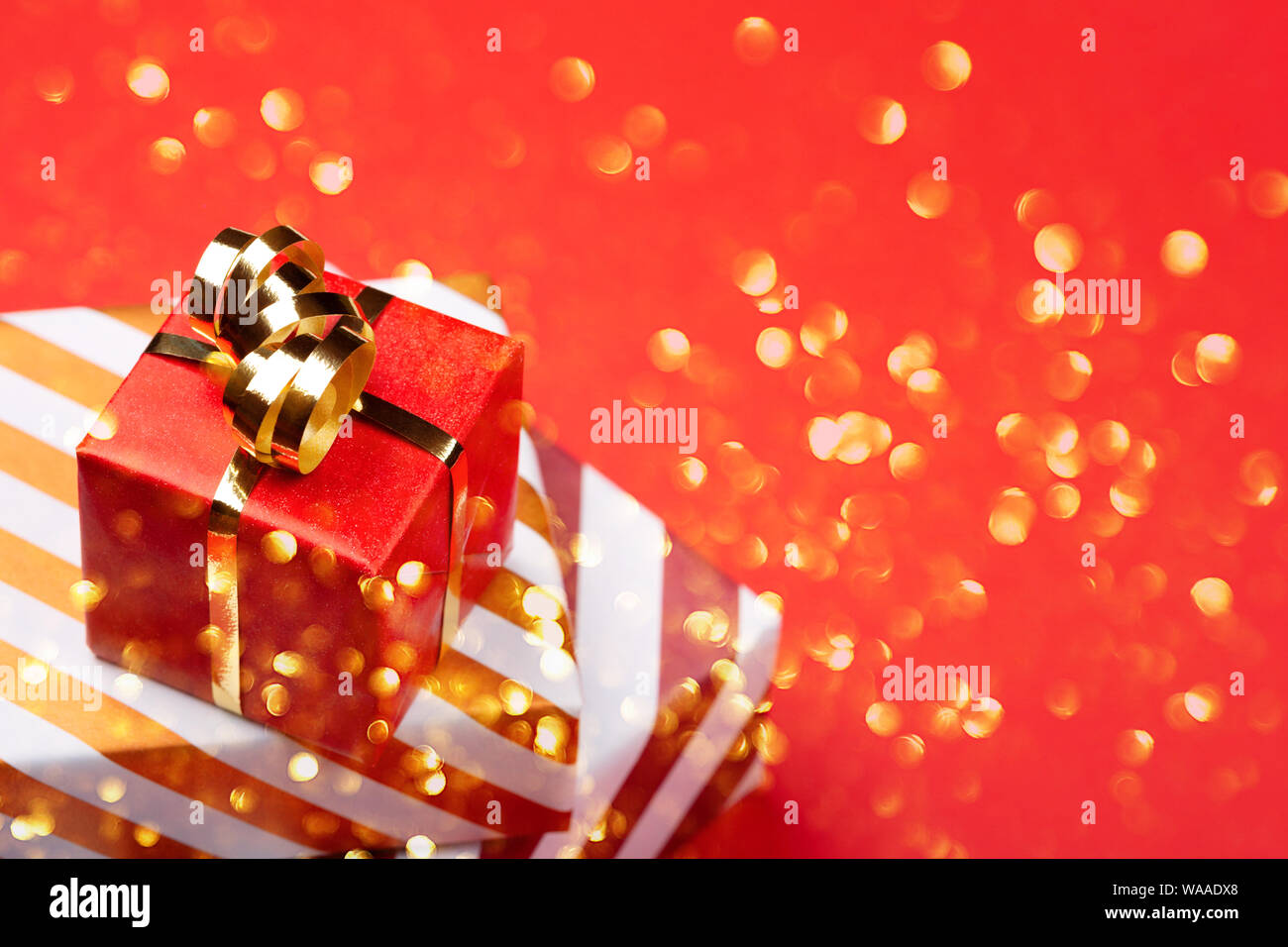 Confezioni regalo avvolto in rosso e la carta a righe con golden bow su sfondo rosso. Natale e vacanze in stile minimale biglietto di auguri con coriandoli. Foto Stock