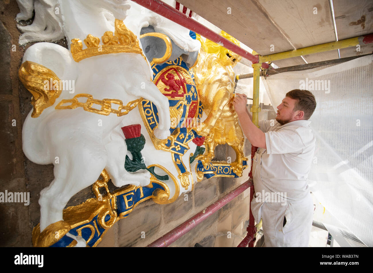 Colin Morris, da Nevin di pittori di Edimburgo, si applica la foglia di oro a uno dei royal stemmi durante i lavori di ristrutturazione sulla facciata principale di Canongate Kirk di Edimburgo. Foto Stock