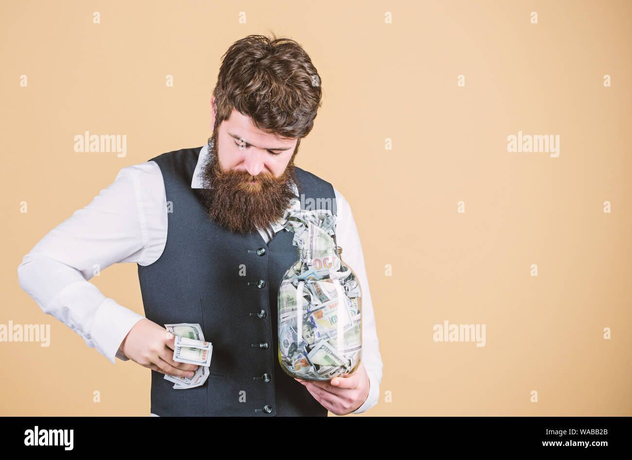 Ripieno di un po' di denaro nelle sue tasche. Uomo Barbuto nascosti e tesoreria. Imprenditore prendendo denaro contante al di fuori del vaso di vetro. Il flusso di cassa di bilancio, copia dello spazio. Foto Stock