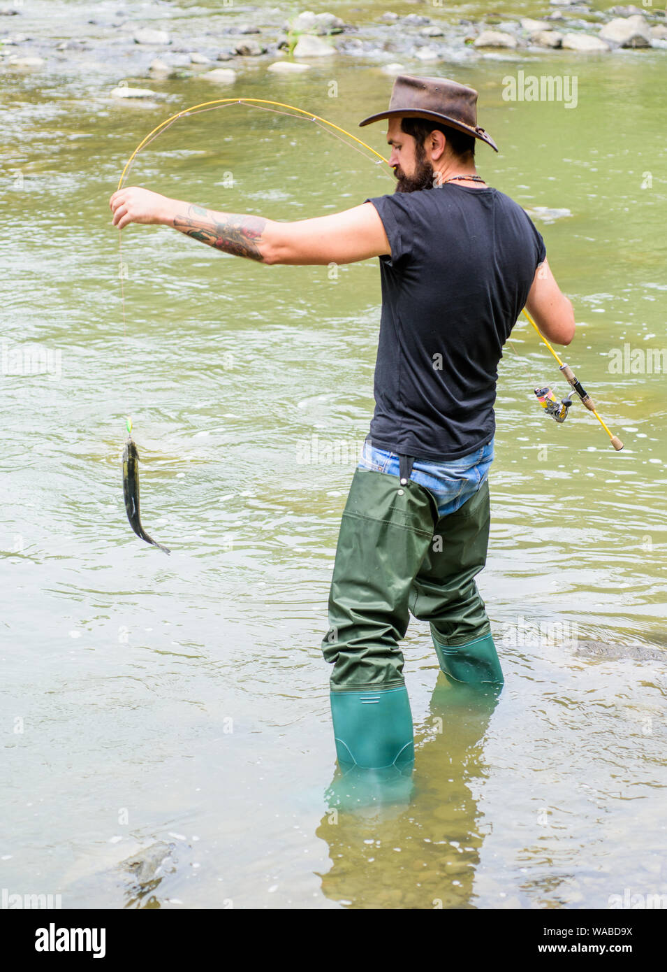 Pesca hobby maschile. Uomo brutale indossare stivali di gomma riposare in  acqua di fiume. Weekend di Fisher attività. Fisher con attrezzature da pesca.  Pesce sul gancio. Tempo libero nella natura selvaggia. Divertimento