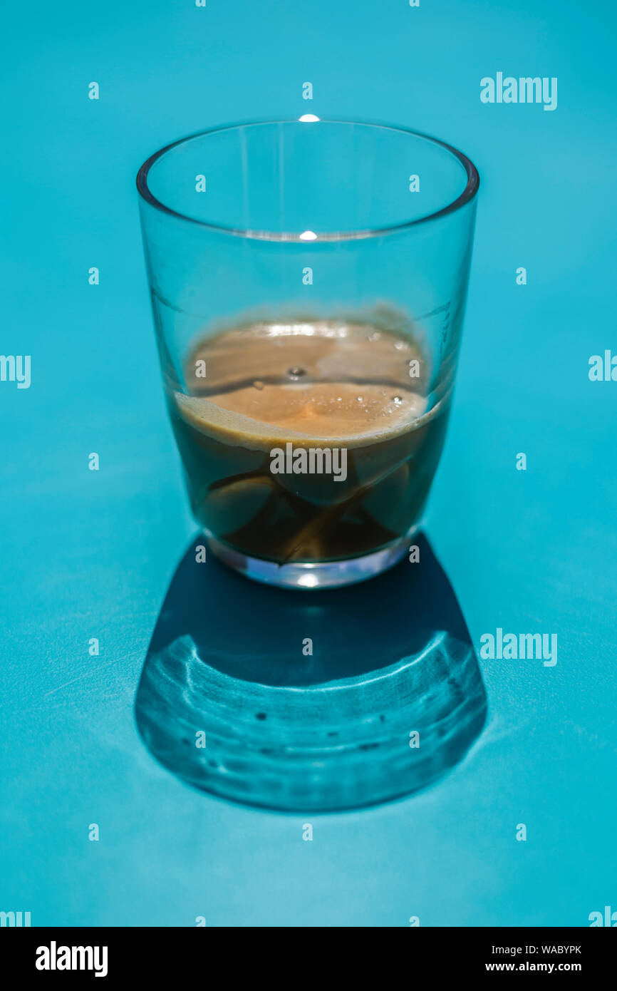 Un bicchiere piccolo di caffè nero su un tavolo blu Foto Stock