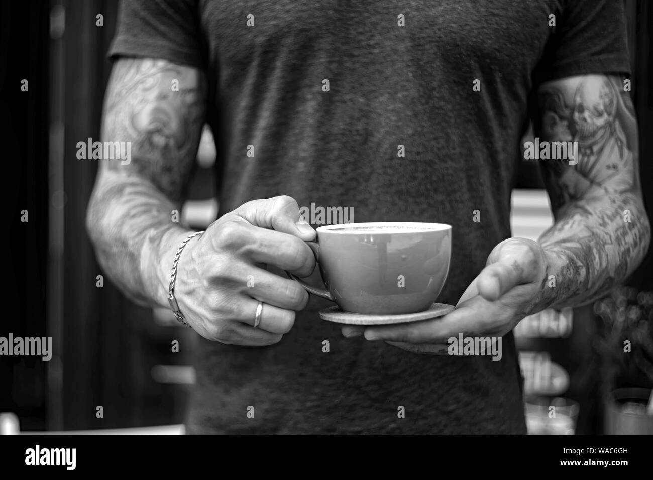Close up dell uomo che serve caffè permanente, mentre in coffee shop. Concentrarsi sulle mani maschio posizionando una tazza di caffè per il contatore. Foto Stock