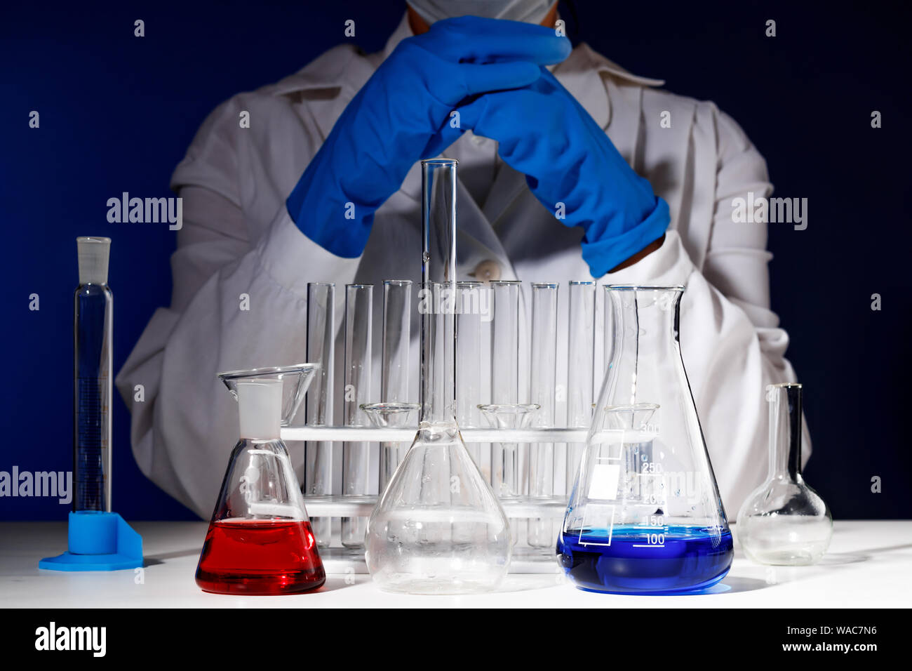 In un laboratorio di chimica, un farmacista femmina è seduta al tavolo circondato da tubi di prova. Esperimento medico. Farmacia lavorando su una prova con guanti blu Foto Stock