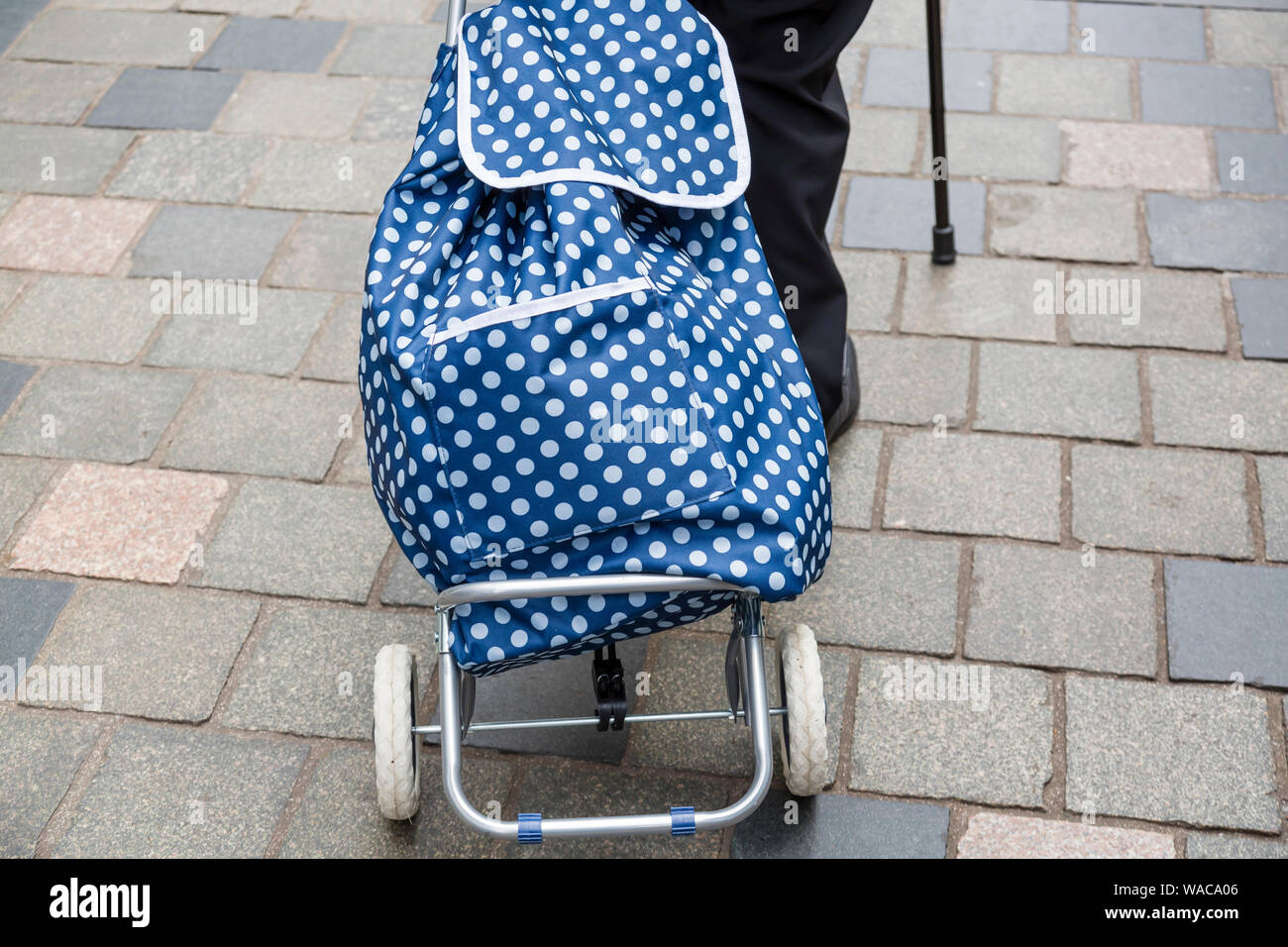 Signore anziano che usa un bastone da passeggio e tira una borsa per la spesa su ruote, Scozia, Regno Unito Foto Stock