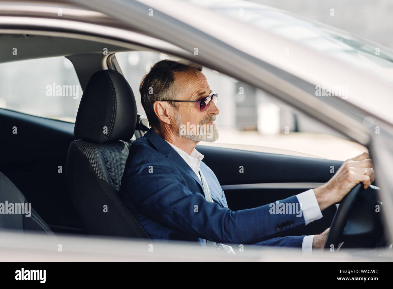 Imprenditore senior alla guida di una vettura. Vista laterale di un uomo in abbigliamento formale seduti nel veicolo. Foto Stock