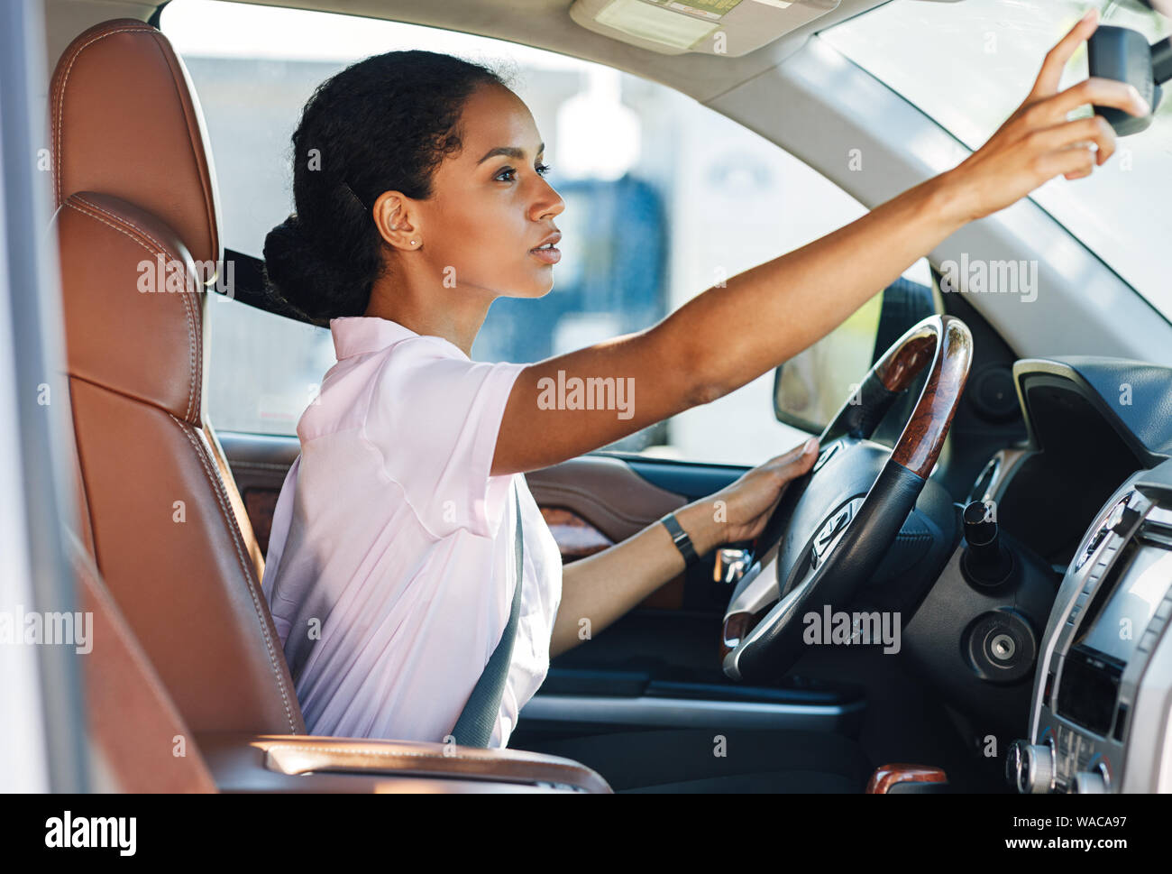 Vista laterale della donna regolazione dello specchietto retrovisore mentre si è alla guida di un veicolo Foto Stock