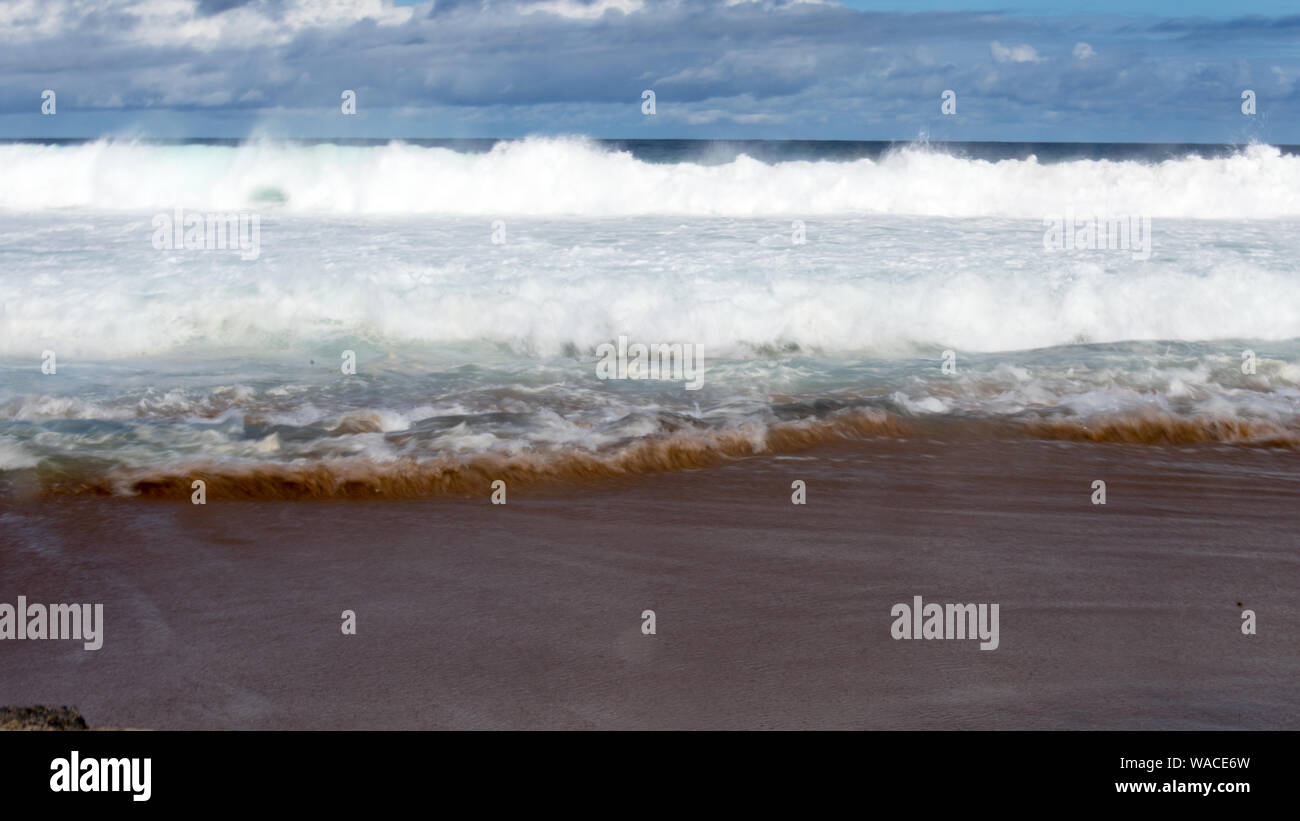 Marea. Vicious onde con la marea di schiantarsi contro il litorale con una forte risacca. Il surf è schiumoso su un nuvoloso giorno. Foto Stock