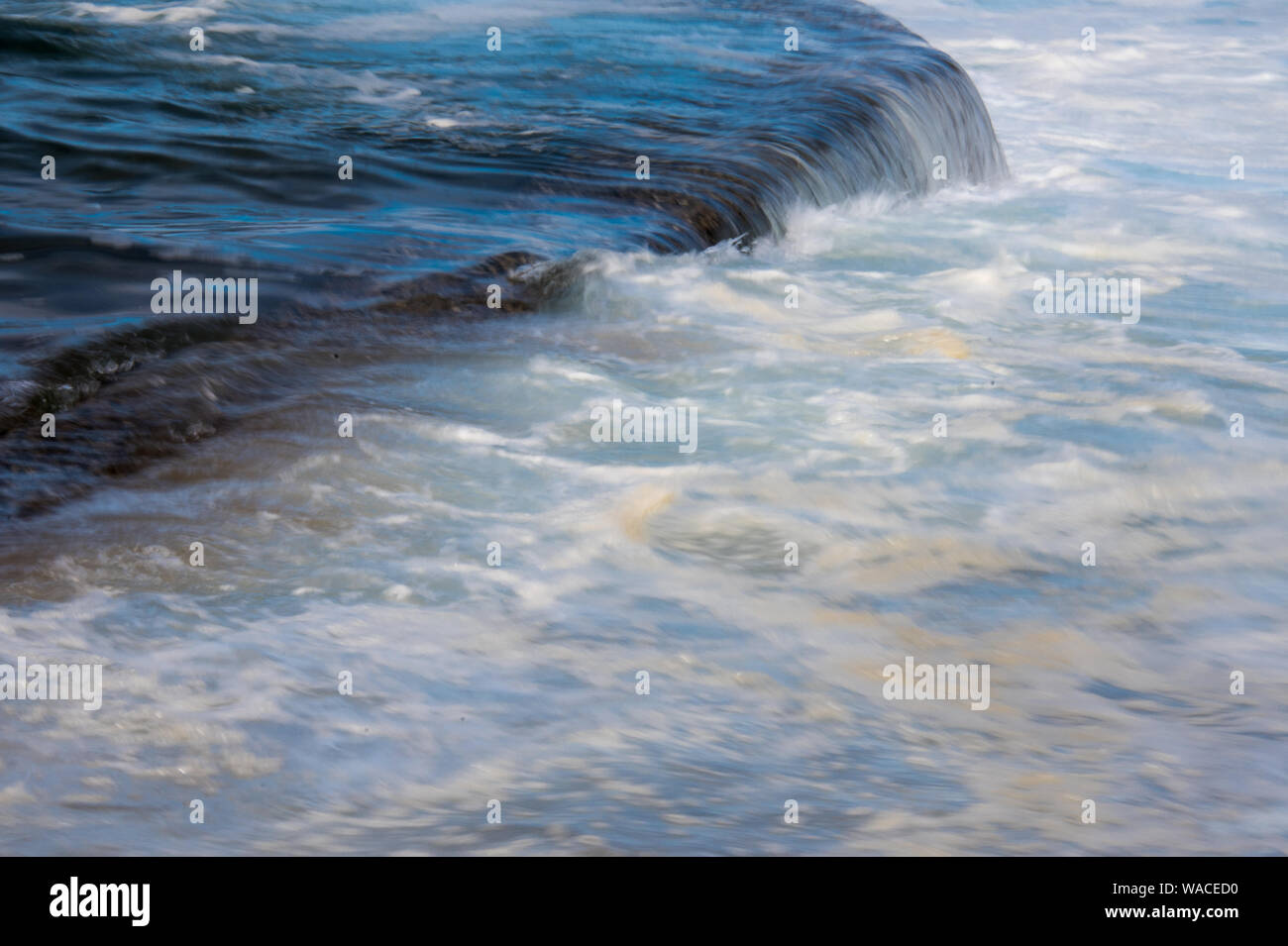 Marea. Vicious onde con la marea di schiantarsi contro il litorale con una forte risacca. Il surf è schiumoso su un nuvoloso giorno. Foto Stock