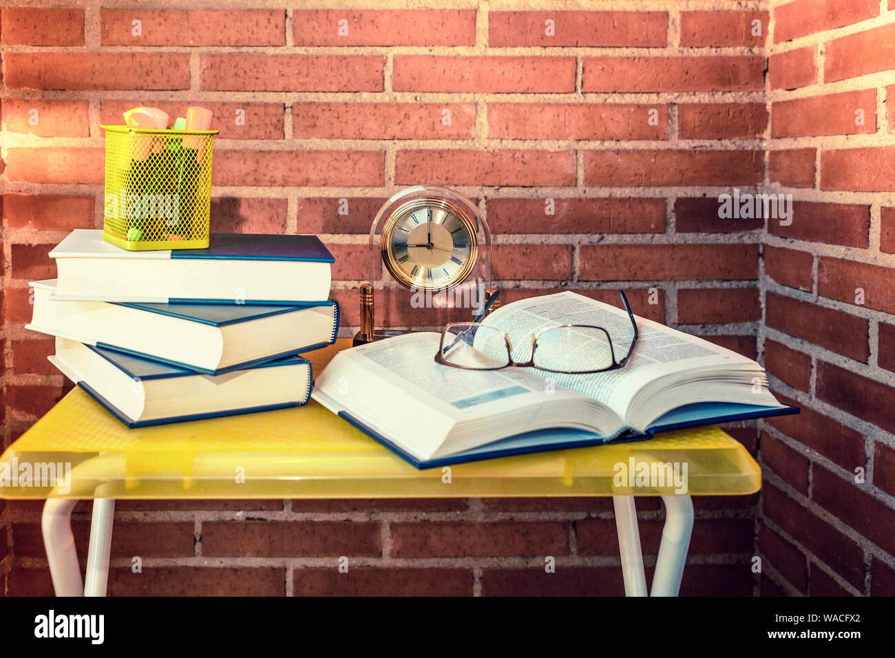 Vista di libri e occhiali sulla tabella di colore giallo con un muro di mattoni di sfondo il tempo di apprendimento Foto Stock