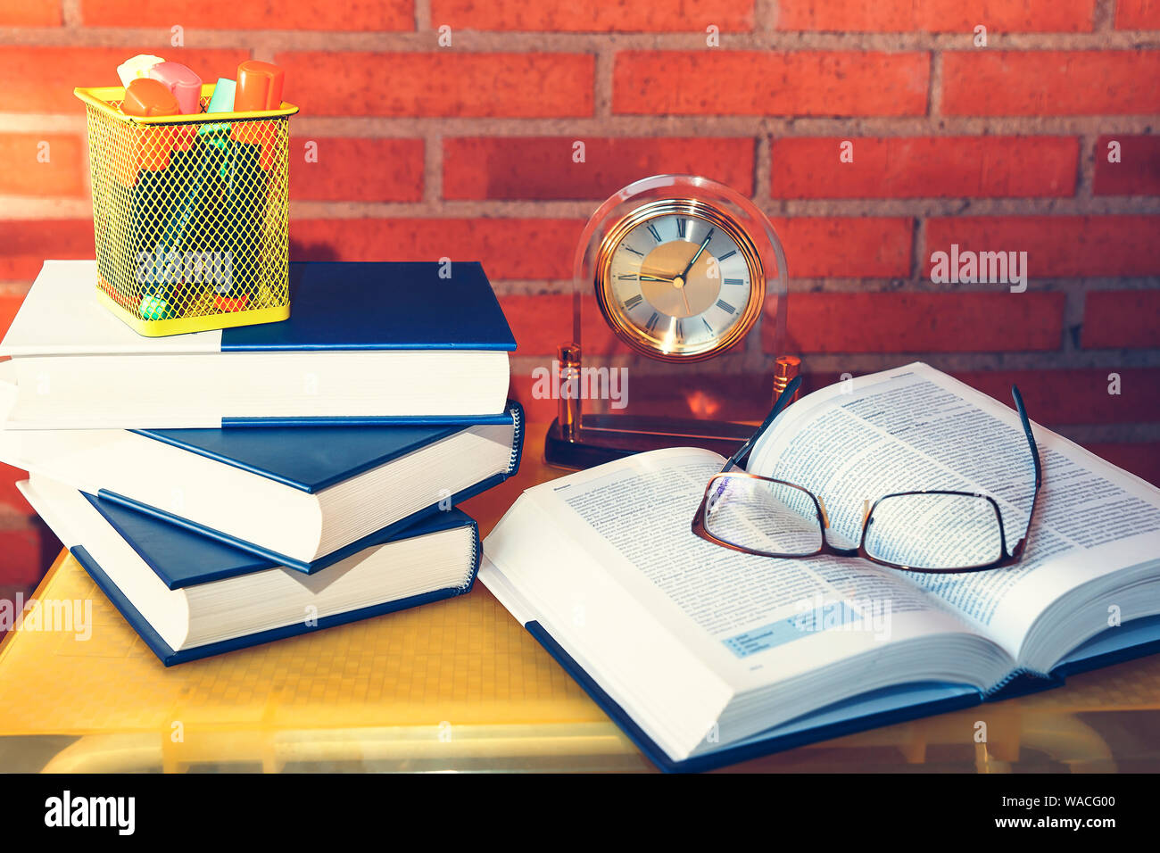 Occhiali su un libro aperto su una tabella di colore giallo di fronte a un muro di mattoni Foto Stock