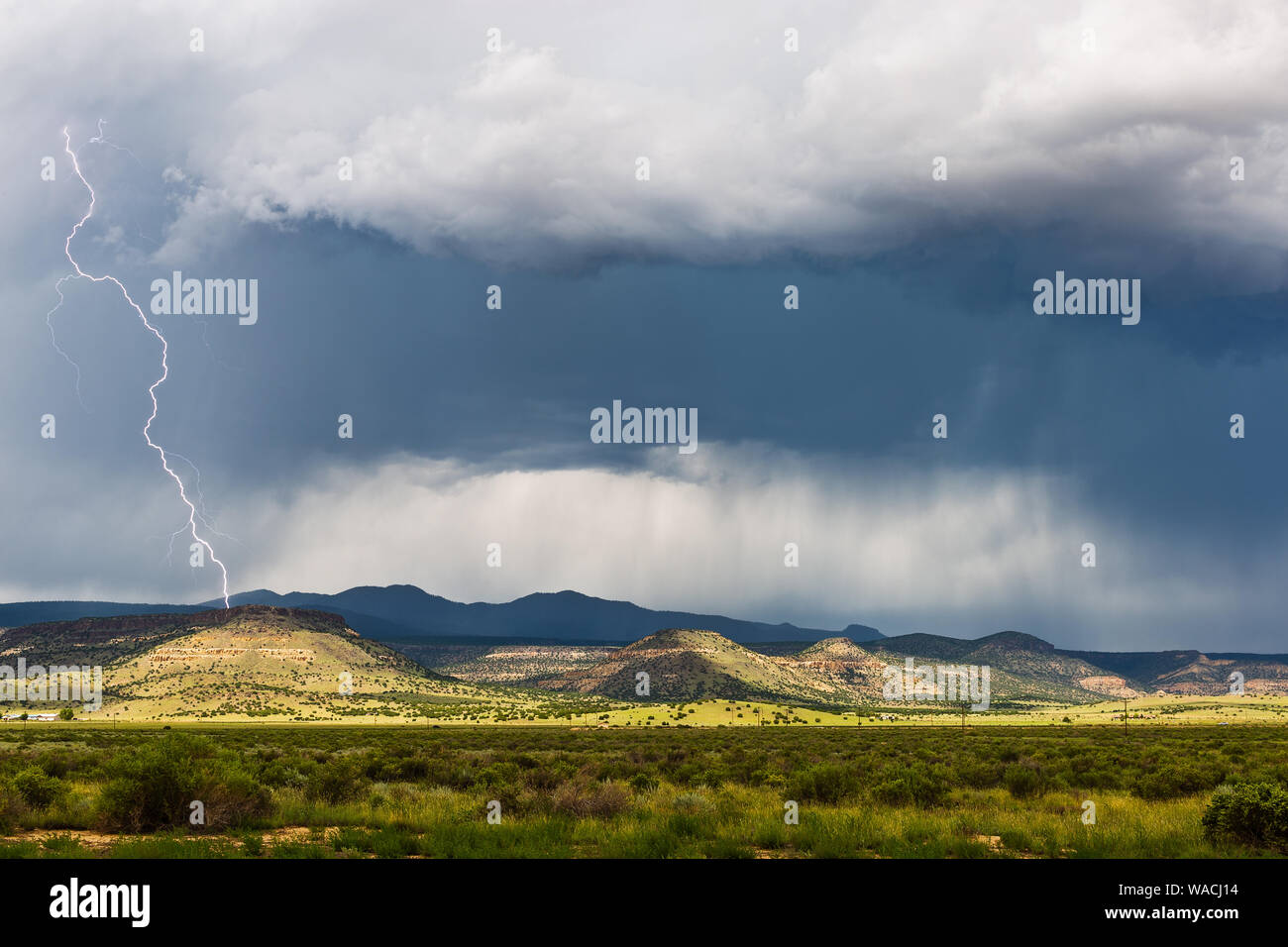 Temporale con fulmine e luce solare su montagne lontane vicino a Grants, New Mexico, USA Foto Stock