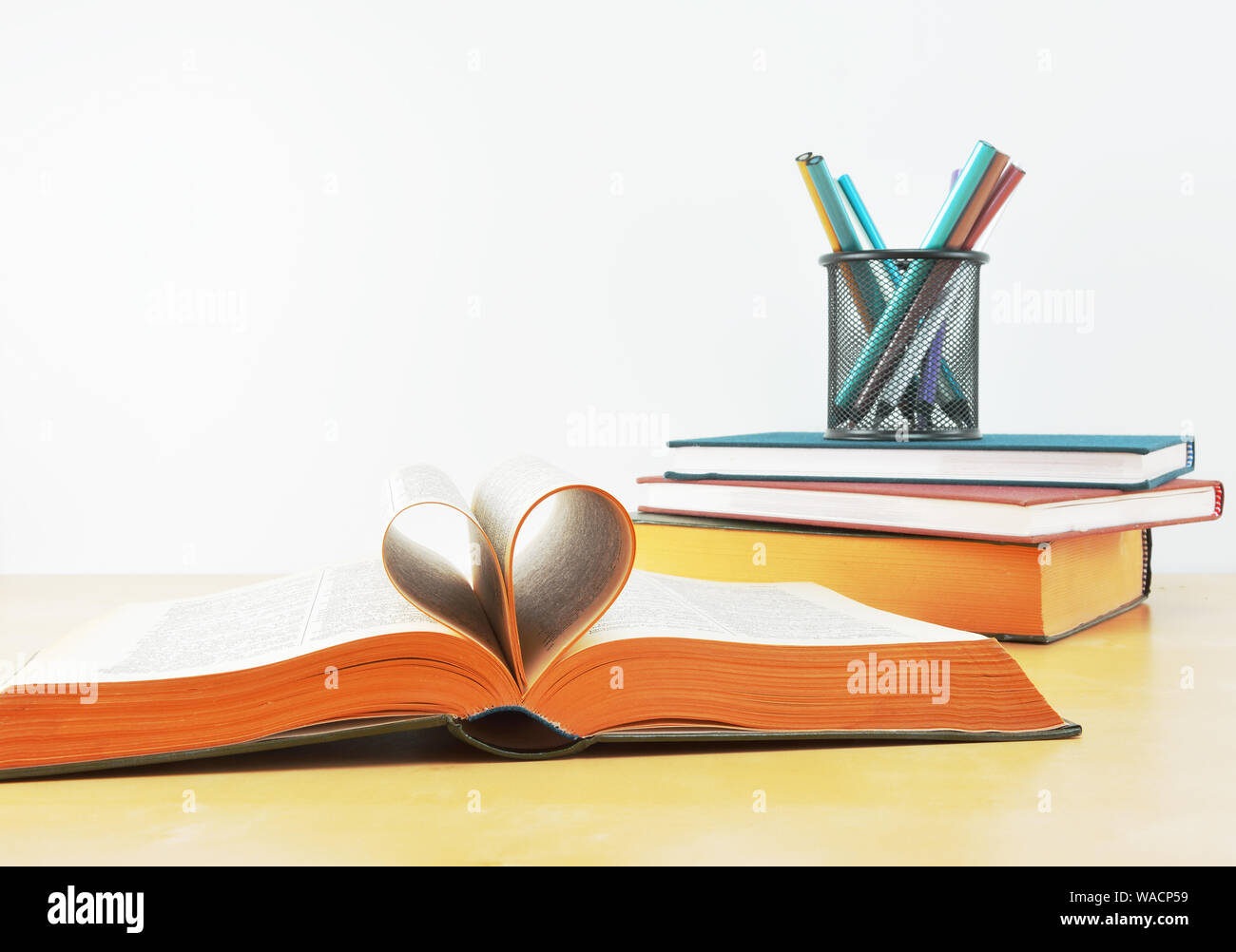 Amore il concetto di scuola con le pagine del libro formata in forma di cuore,libri e portamatite con matite colorate Foto Stock