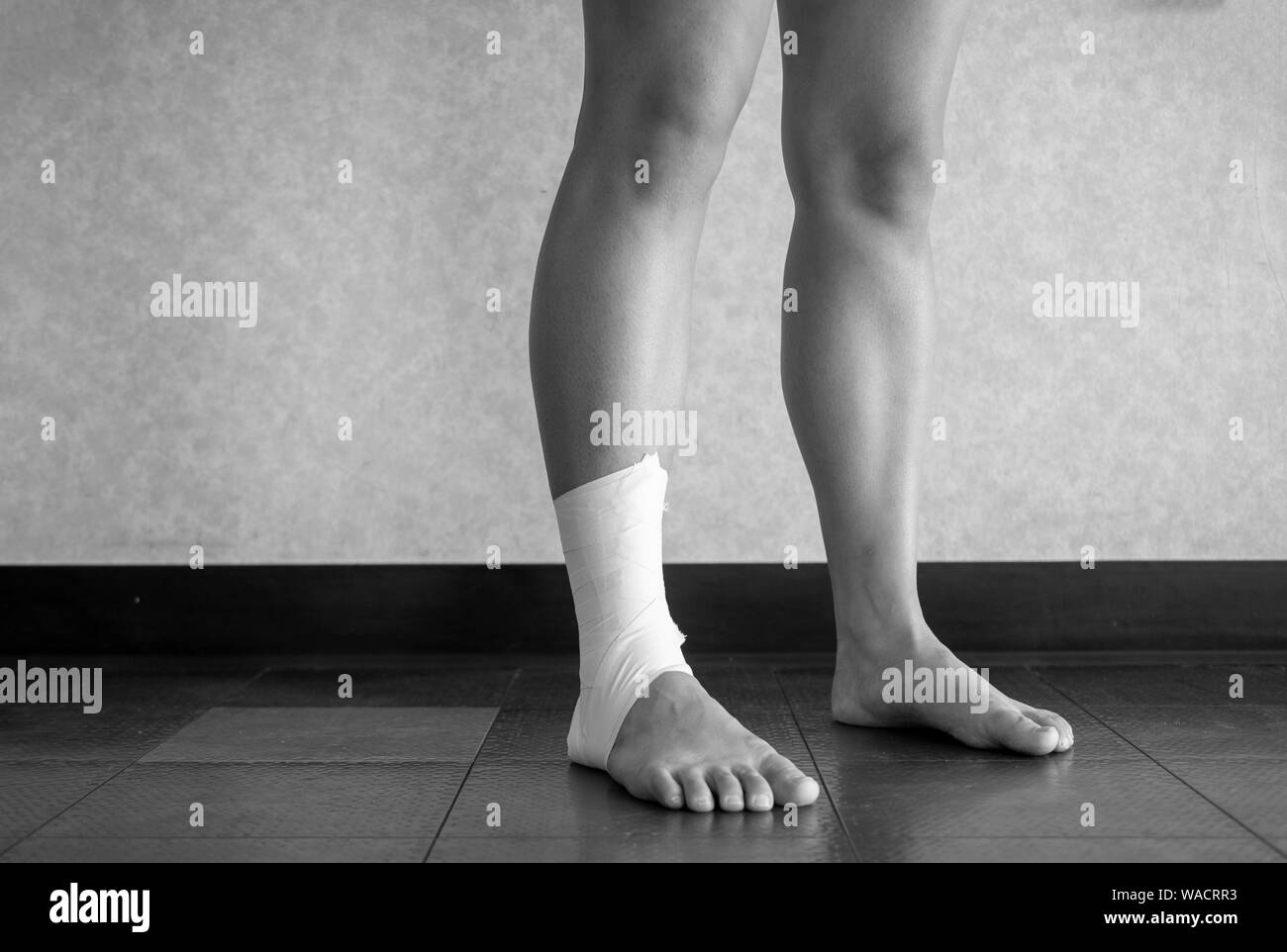 Versione in bianco e nero di atleta in piedi con un nastro di caviglia lavoro sulla loro caviglia infortunata Foto Stock