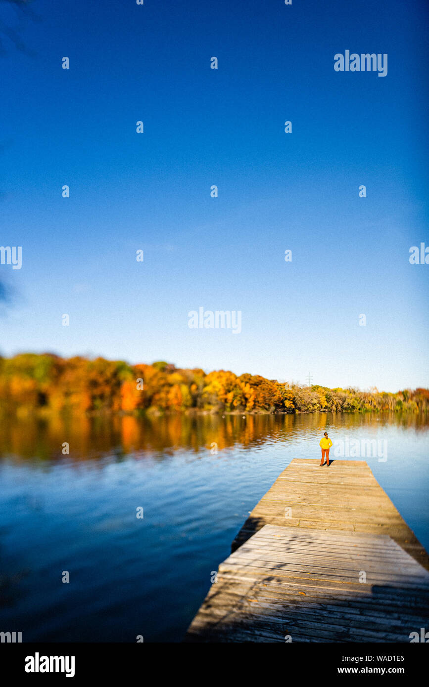 Giovane donna in piedi sul molo vicino al fiume con i colori dell'autunno Foto Stock