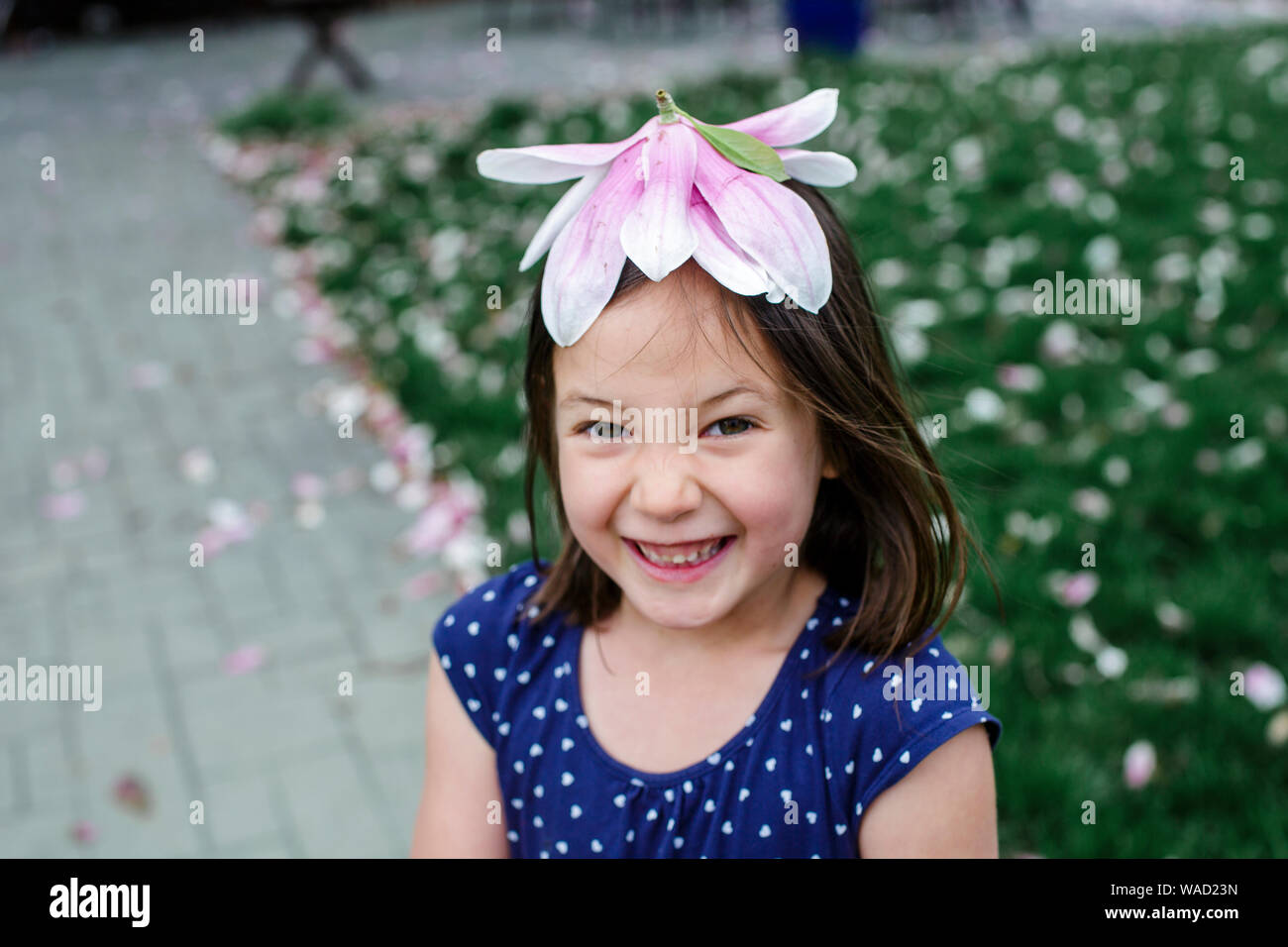 Un sogghignando bambina indossa un fiore di magnolia per un cappello Foto Stock