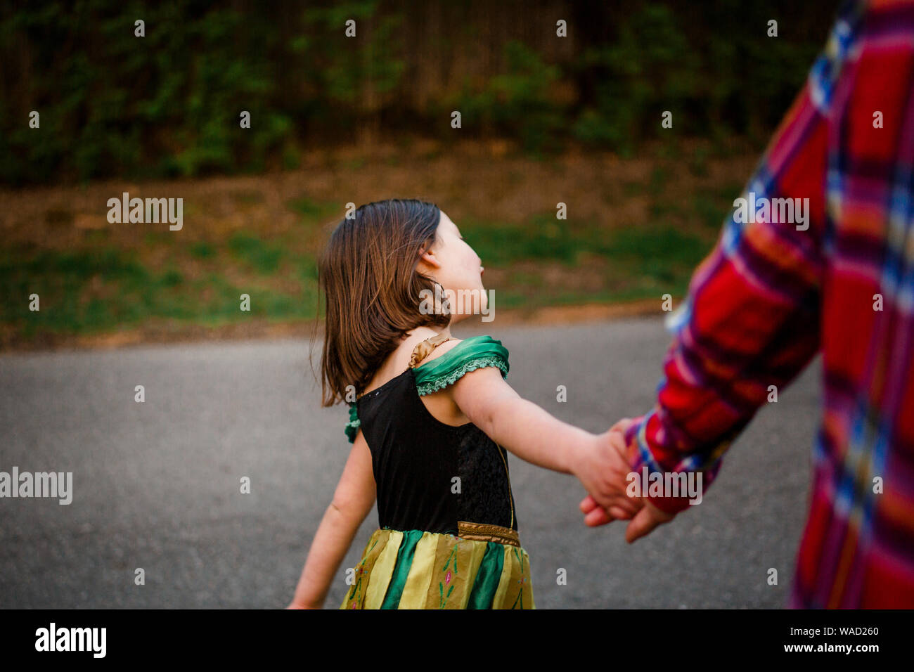 Un piccolo bambino in un costume principessa trattiene il suo padre le mani su una passeggiata Foto Stock