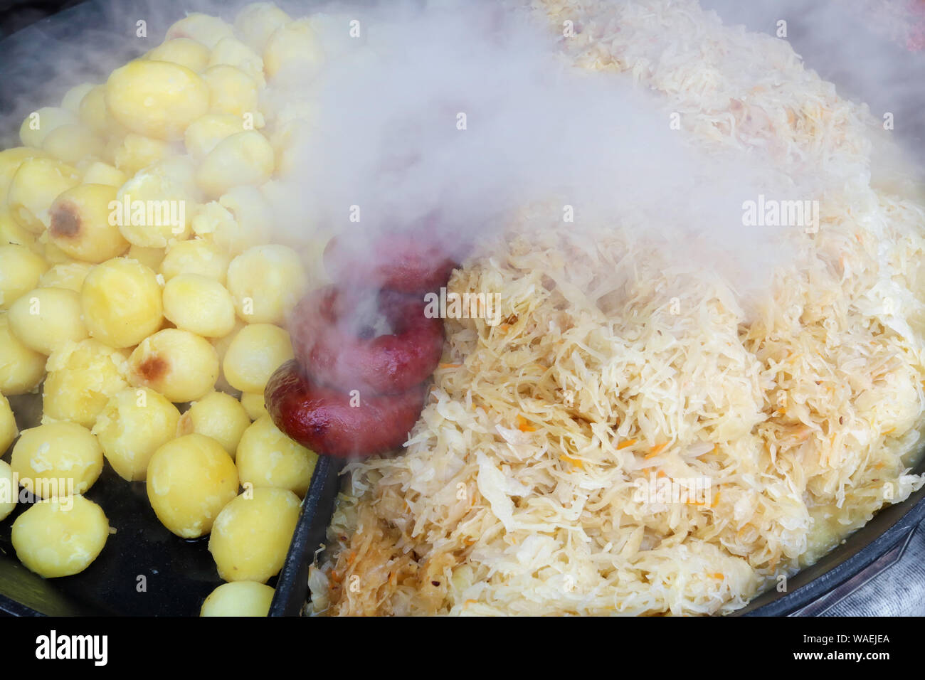 Via fast-food - affumicate Salsicce di maiale fritto di patate e cavolo in grande nero ferro padella. Snapshot immagine di stile Foto Stock