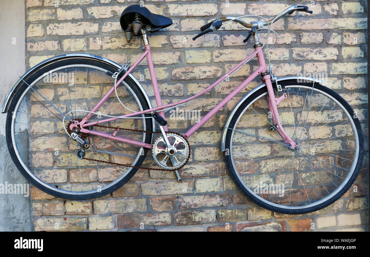 Vecchio arrugginito rotto donne rosa's bike appeso su un mattone giallo  parete Foto stock - Alamy