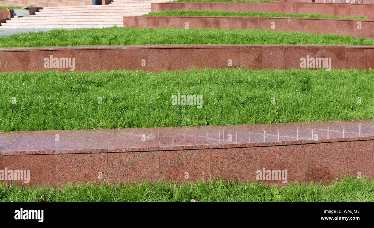 Prospettiva di passi effettuati di granito rosso di pietra e fresco verde erba. Panoramica sullo sfondo all'aperto Foto Stock