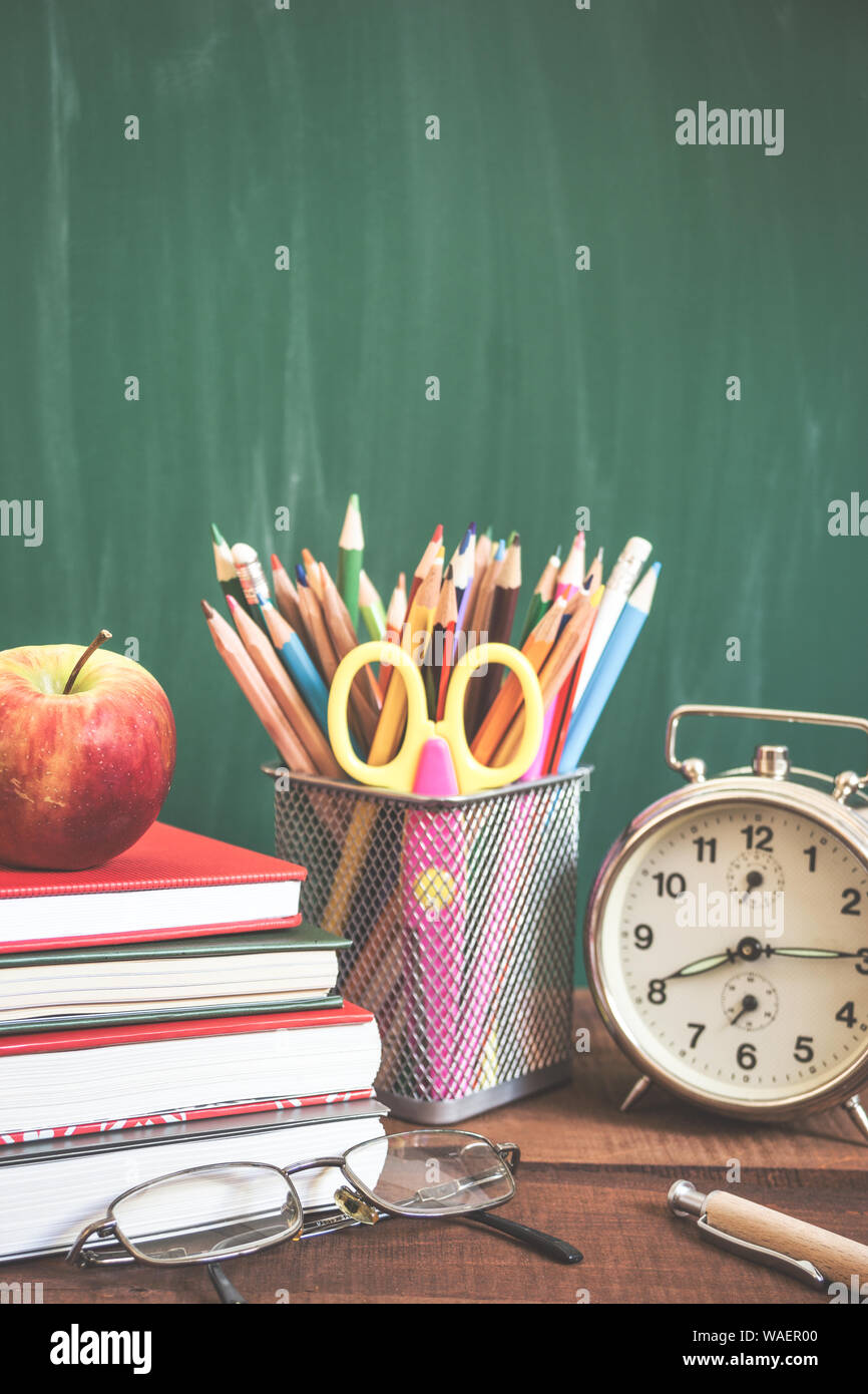 Forniture scolastiche, sveglia, Apple e i libri sul tavolo di legno davanti alla scuola lavagna. Si torna a scuola concetto. Vintage foto dai toni. Foto Stock