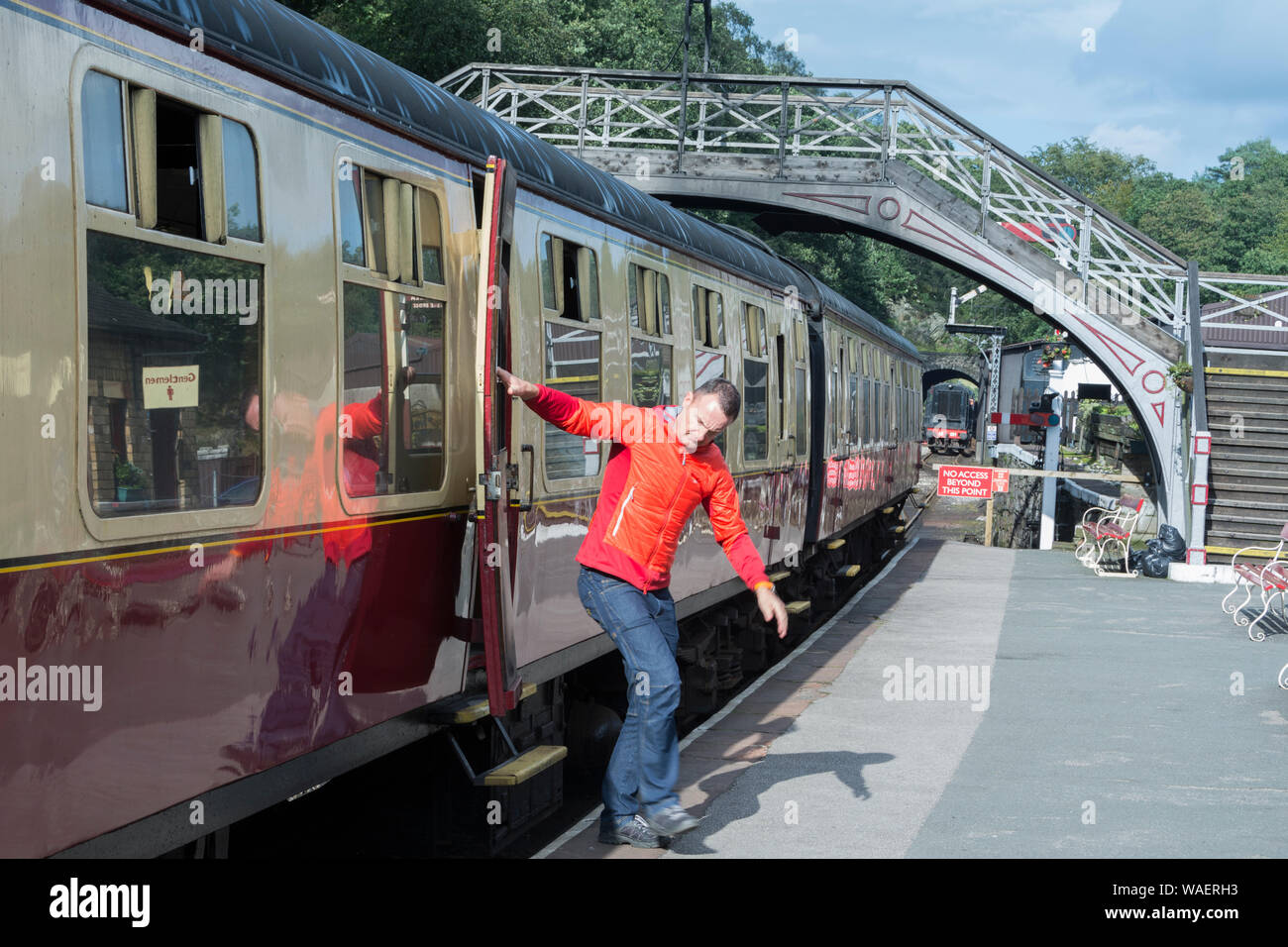 Uomo salta fuori da un treno alla stazione di Haverthwaite sul lungolago e Patrimonio Haverthwaite Railway vicino a Ulverston, Cumbria, Regno Unito Foto Stock