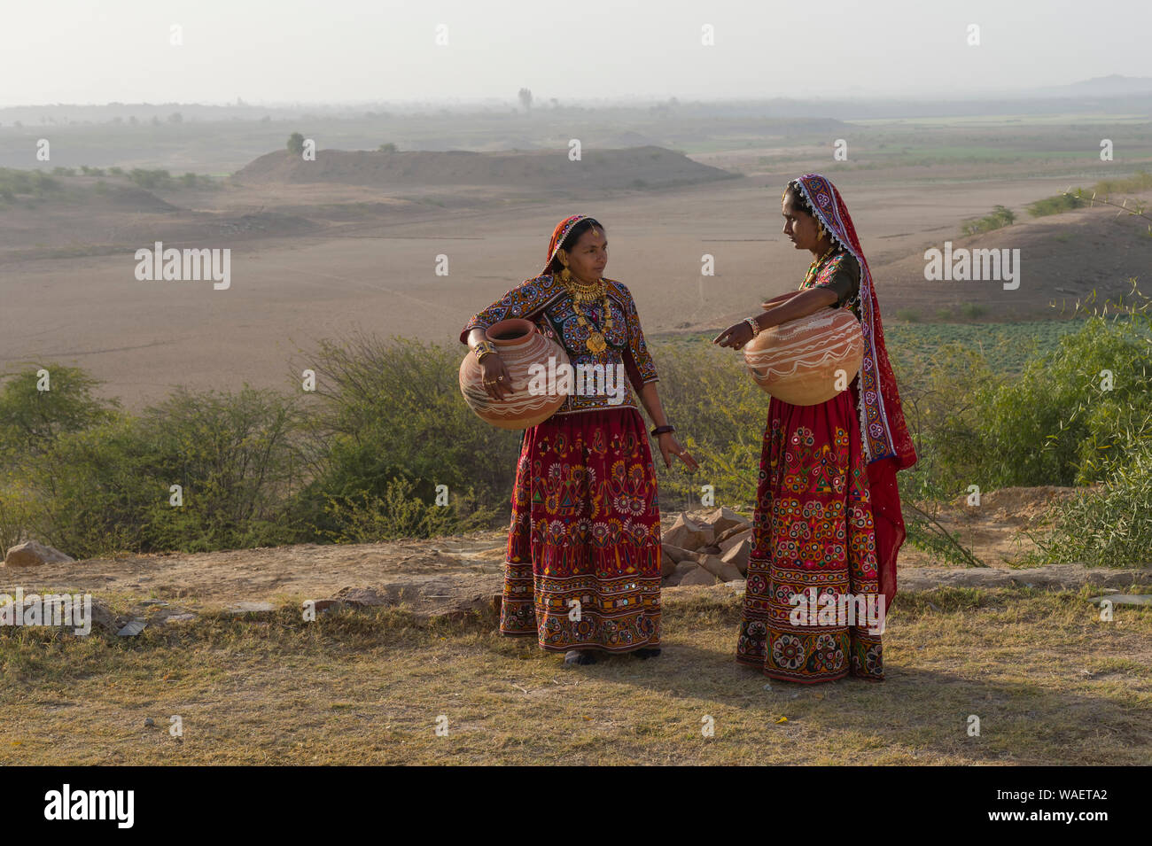 Due donne Ahir nel tradizionale tessuto colorato che trasportano acqua in una brocca di argilla, grande Rann di Kutch deserto, Gujarat, India Foto Stock