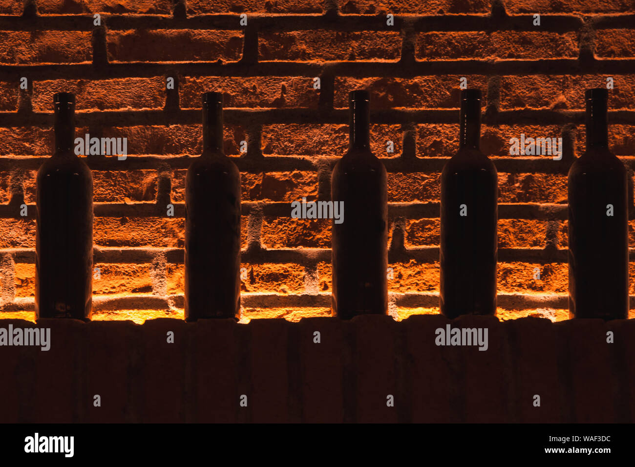 Polverose bottiglie di vino stand in una fila su un ripiano in un archivio di vino rosso con un muro di mattoni su uno sfondo Foto Stock