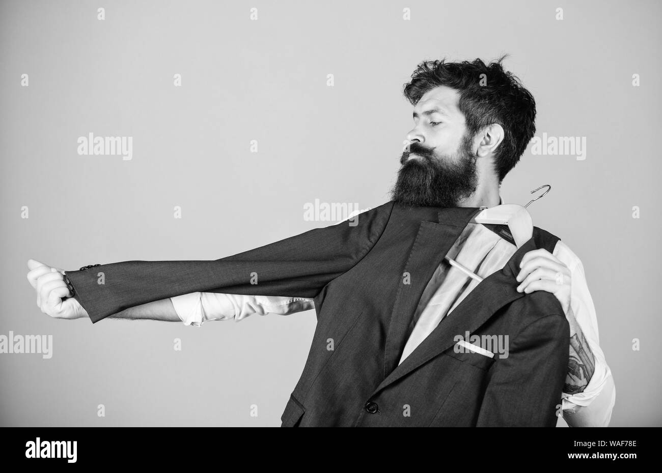 A casa su misura. Maestro sarto. Uomo Barbuto misurando la lunghezza del manicotto di tuta giacca in sartoria. Hipster holding tailor made rivestire al department store. Abbigliamento e sartoria. Foto Stock