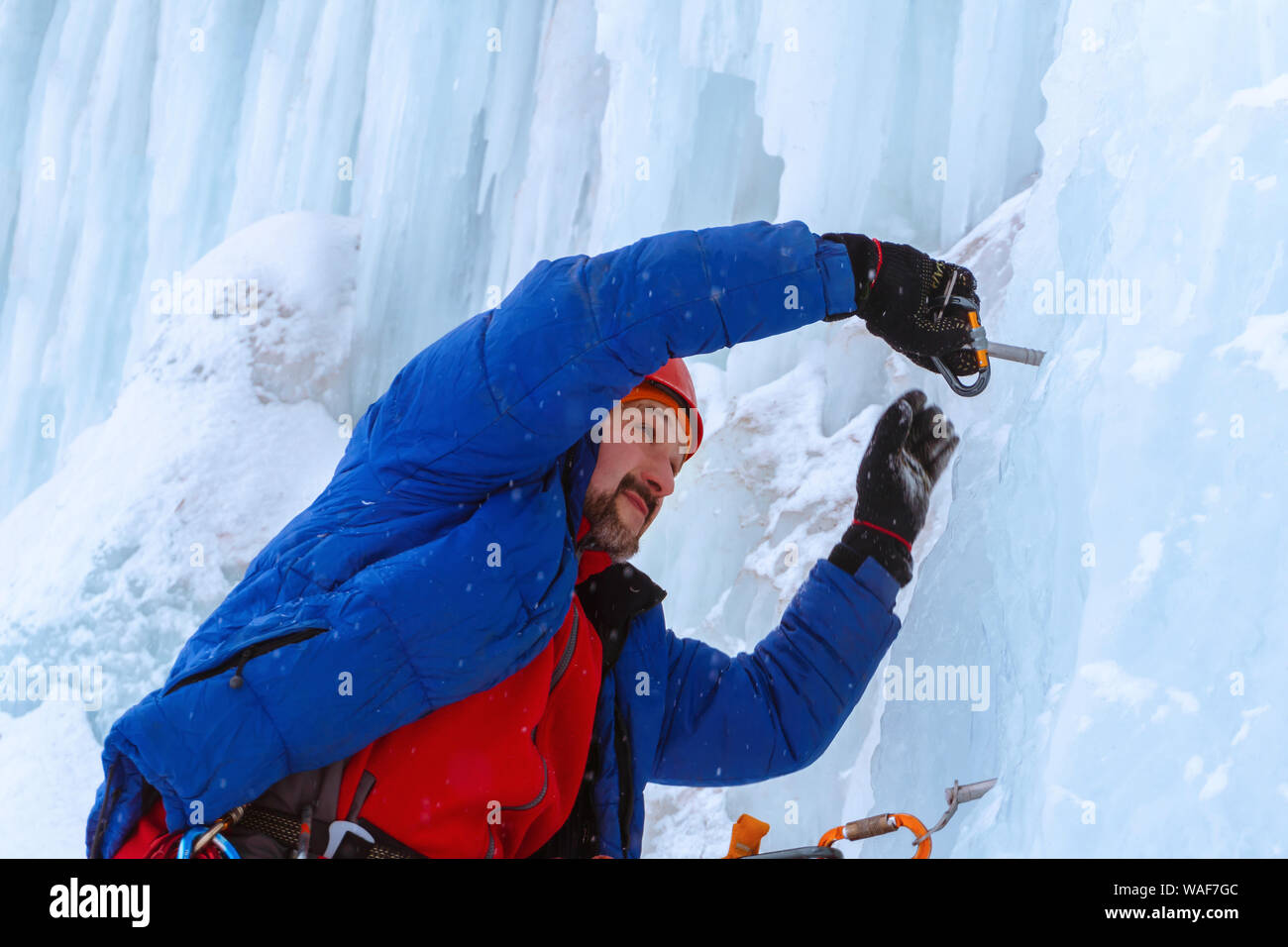 Ice Climber preraring acceso sosta avvitando la vite di ghiaccio nella parete del ghiacciaio Foto Stock