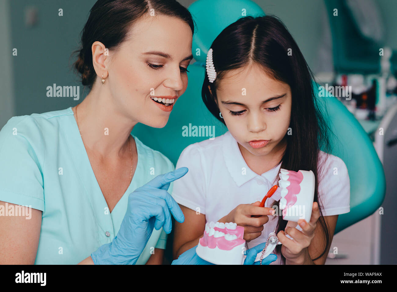 Sorridente razza mista ragazza con Dentista pediatrico che mostra di spazzolatura giusto modo spazzolando i denti Foto Stock