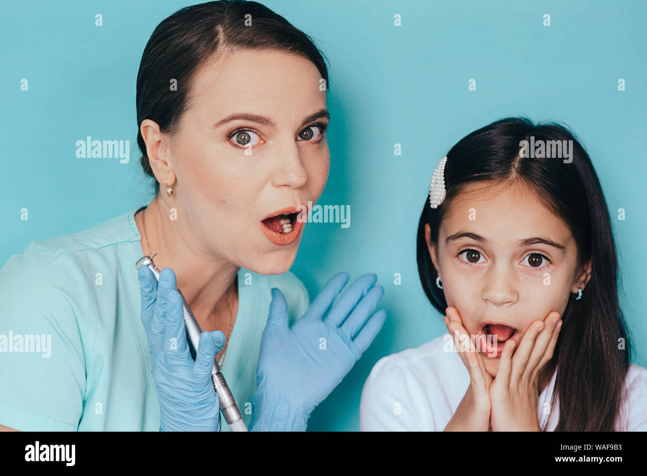 Bambino denti trattamento . po' di razza mista ragazza e dentista scioccato emozione con trapano dentistico su sfondo blu Foto Stock