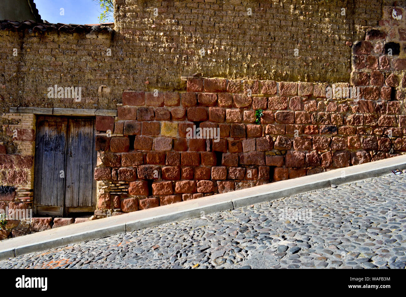 Strada in discesa con la facciata in mattoni rossi con una porta in Sucre, Bolivia Foto Stock