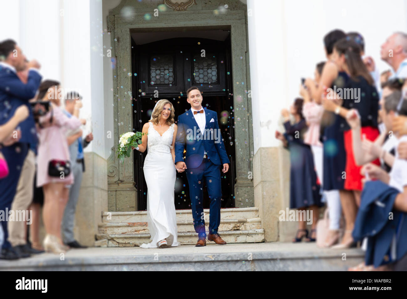 Sposi novelli kissing mentre si esce dalla chiesa dopo la cerimonia di  matrimonio, la famiglia e