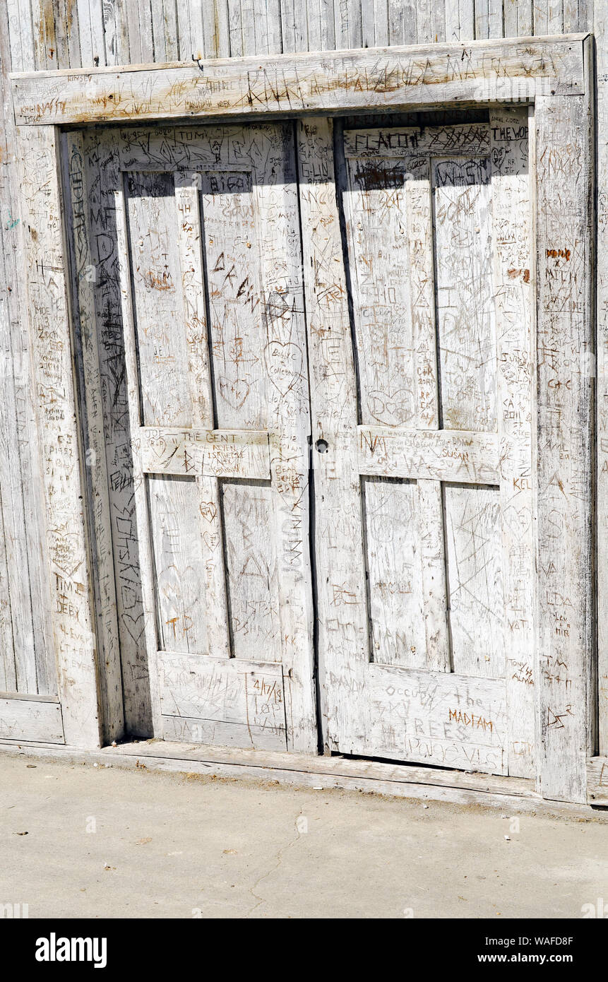 Porte in legno intemperie che pende sul marciapiede con iniziali intagliate su tutta la superficie, Locke, California Delta, California, USA Foto Stock