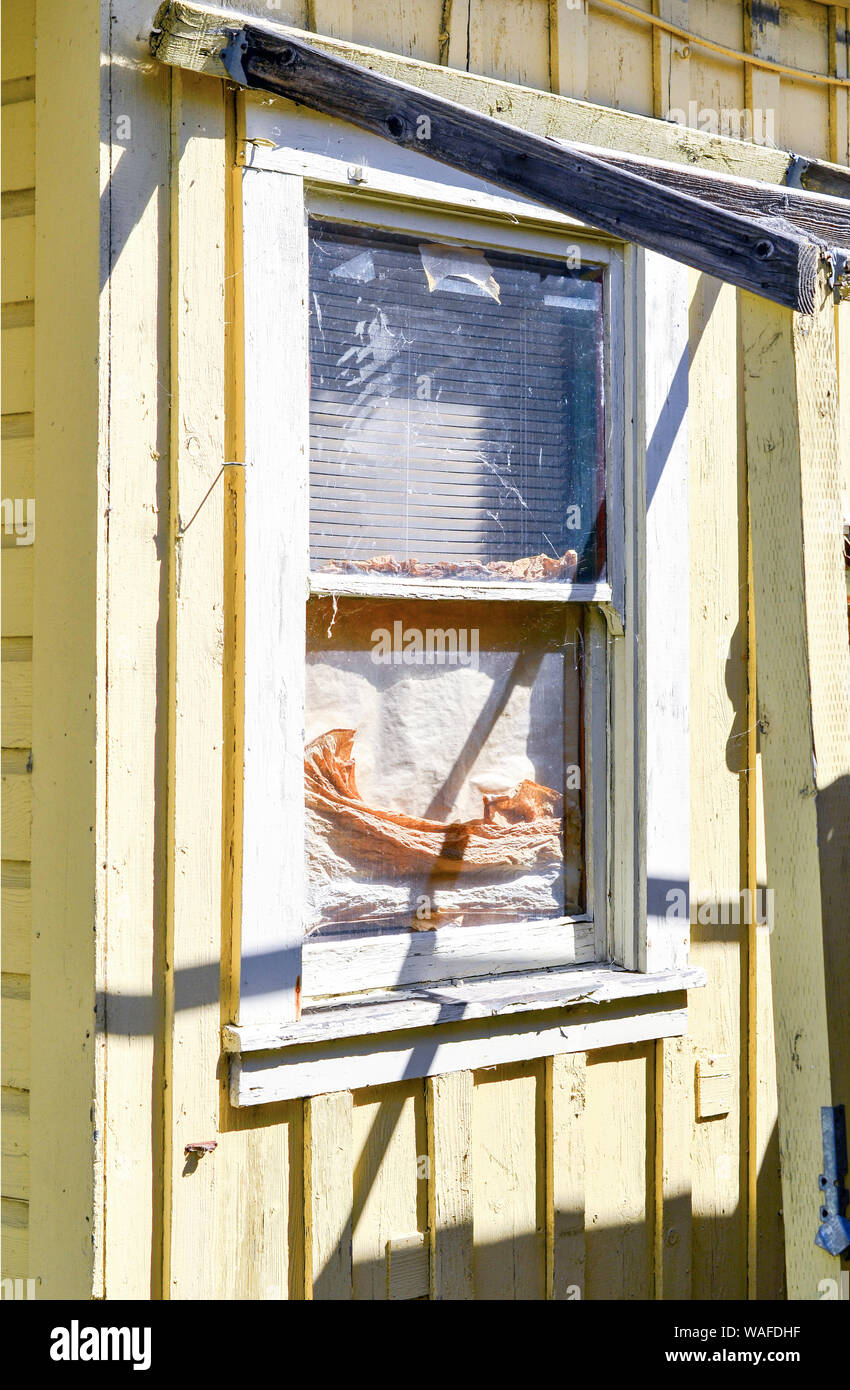 Appeso doppia finestra in legno dipinto di bianco con parzialmente incorniciata tenda sopra circondato da bordo e batten schierata dipinte di giallo Foto Stock