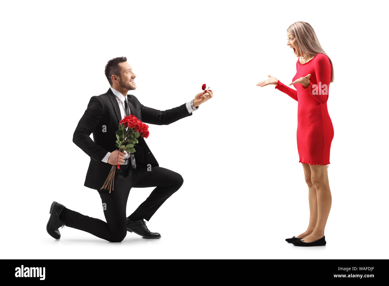 Giovane uomo inginocchiato con le rose e un anello di fidanzamento e proponendo una sorpresa giovane donna isolato su sfondo bianco Foto Stock