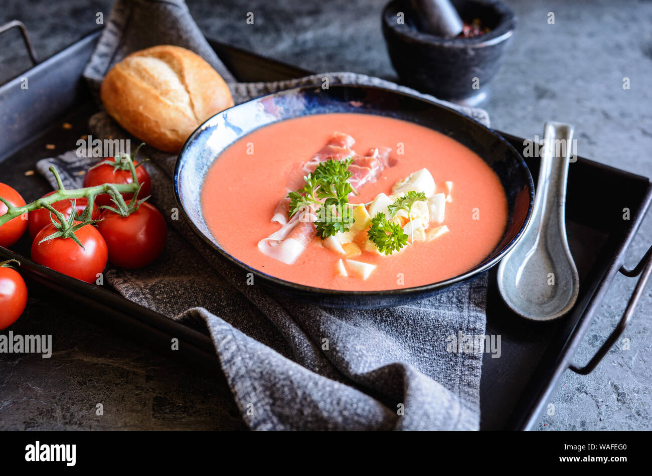 Salmorejo, freddo minestra di pomodoro con prosciutto Serrano e le uova in una ciotola di ceramica, servita con prodotti di pasticceria Foto Stock
