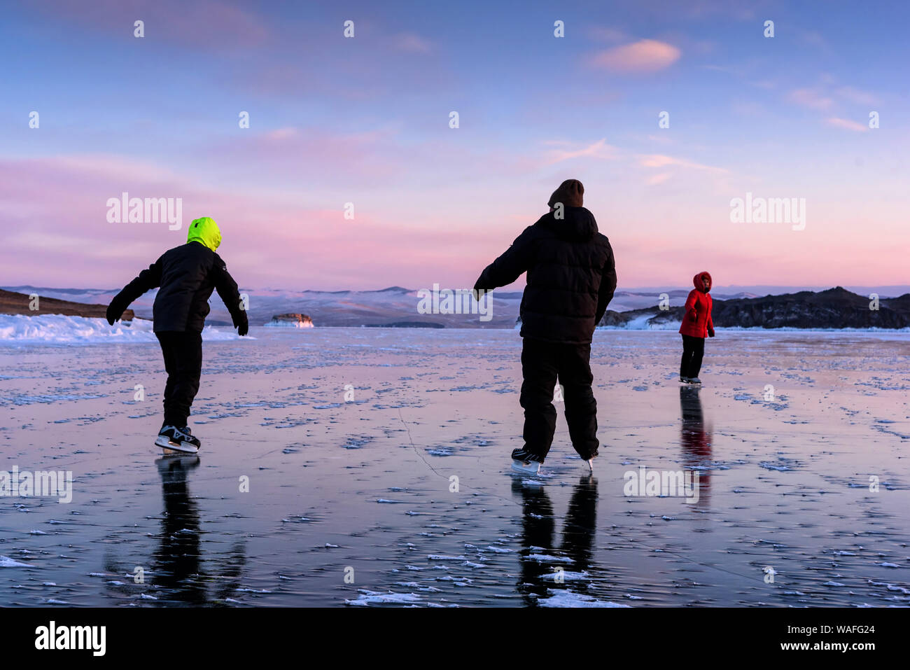 Russia, Sarma - Gennaio 3, 2019: Tre persone pattinaggio sul lago Baikal ghiaccio e hanno un divertimento a luce giallo arancio tramonto di sera d'inverno. Godendo Foto Stock