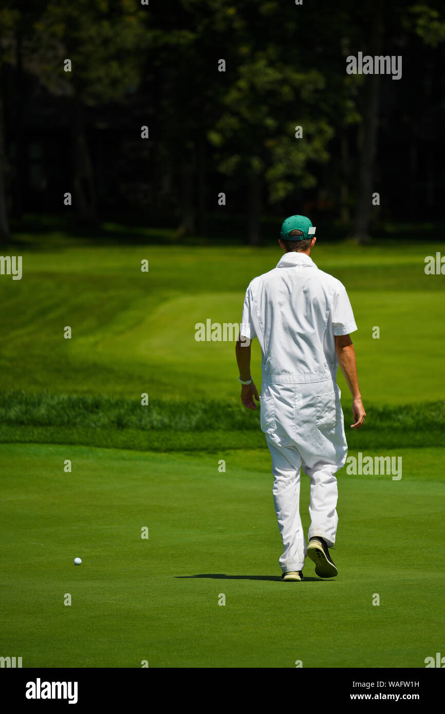 Un campo da Golf non identificato Caddy (Caddie)passeggiate nel verde per consigliare i golfisti di sfide e ostacoli del verde essendo giocato, insieme con i migliori Foto Stock