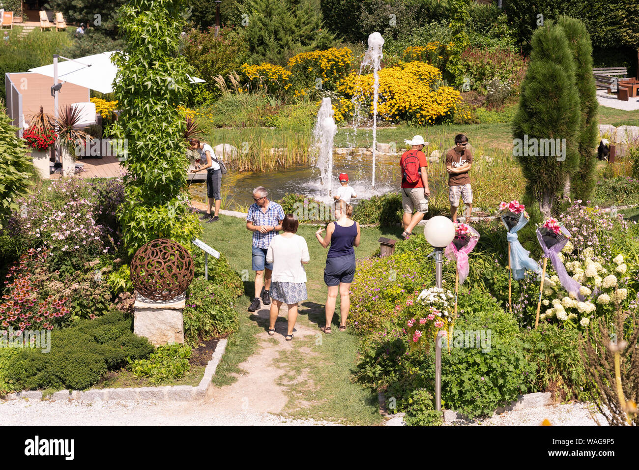 I visitatori di Kittenberger Erlebnisgärten, un famoso giardino botanico in Bassa Austria, godendo le piante, sculture e una fontana in un giorno d'estate Foto Stock