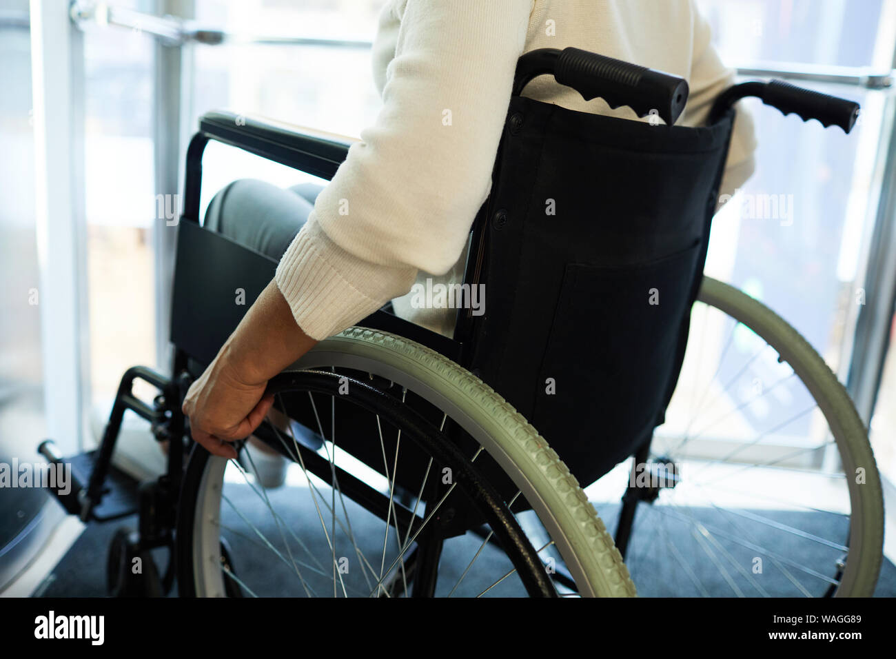 Vista posteriore del senior disabili donna seduta in carrozzina mentre si sta spostando verso il basso l'ascensore Foto Stock